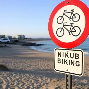 A no-biking sign at Newport Beach with beachgoers in the background.
